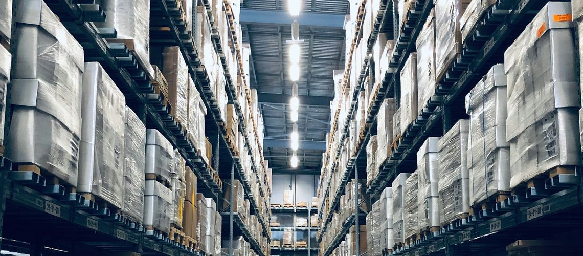Un centre de distribution avec un convoyeur entre des rayonnages remplis de cartons et du personnel réceptionnant les expéditions.