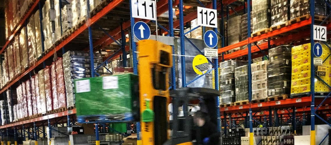 Heftrucks zetten pallets met omwikkelde dozen klaar in een distributiecentrum; op elke pallet hoort een SSCC-label.